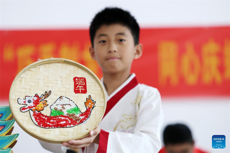 Mtoto akionyesha kazi ya sanaa yenye mchoro wa mashua ya dragoni juu yake katika Wilaya ya Tancheng, Mji wa Linyi, Mkoa wa Shandong, mashariki mwa China, Mei 31, 2025.  (Picha na Zhang Chunlei/Xinhua)